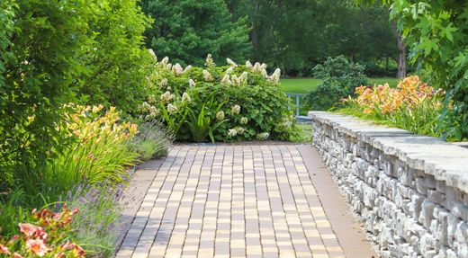 Beispielbild: gepflasterter Gartenweg entlang einer Natursteinmauer mit Staudenpflanzung